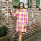Woman in a colorful dress standing in front of a brick building with green shutters.